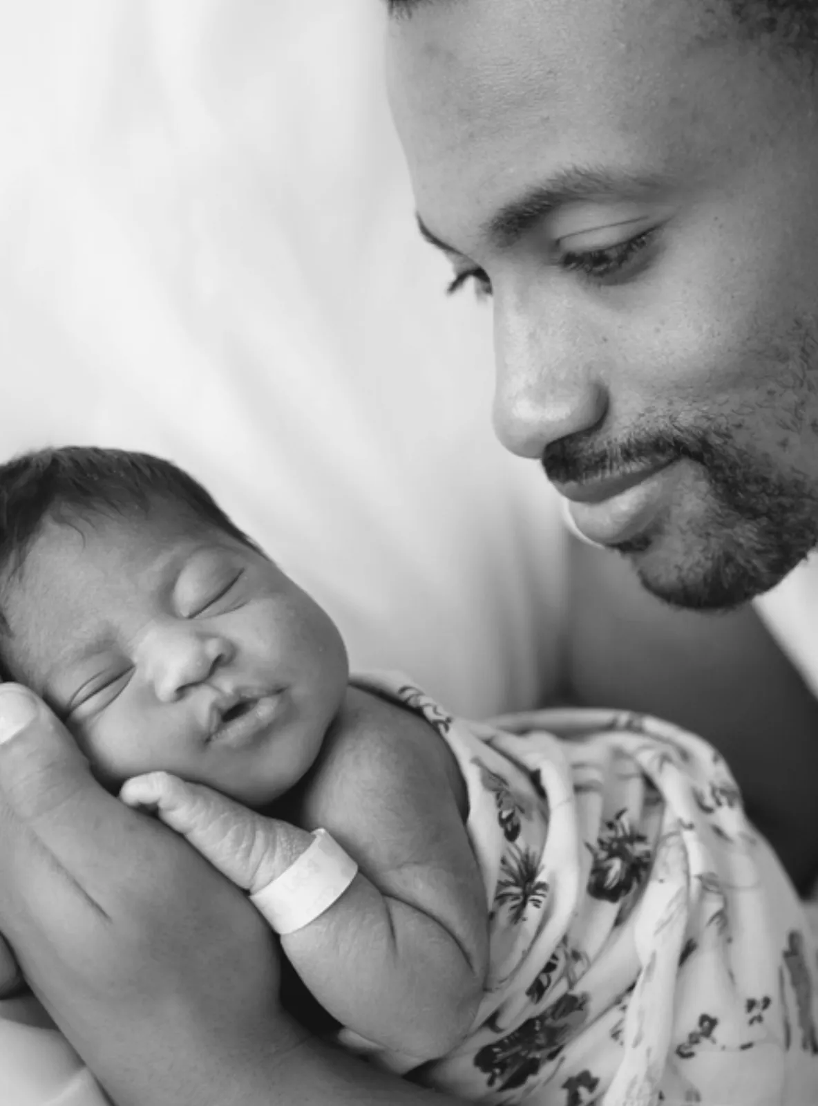 A father smiles down at his sleeping newborn, cradled in one hand